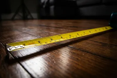 Gros plan sur un mètre ruban posé au sol dans un couloir, symbolisant la mesure de la largeur minimale réglementaire et fonctionnelle.