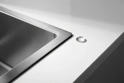 Gros plan sur le joint parfait d'un évier filotop en inox intégré dans un plan de travail en quartz, illustrant la précision du design.
