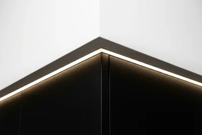 Gros plan sur la jonction parfaite entre un cartongesso blanc et un pensile de cuisine noir, soulignée par une ligne de lumière LED.