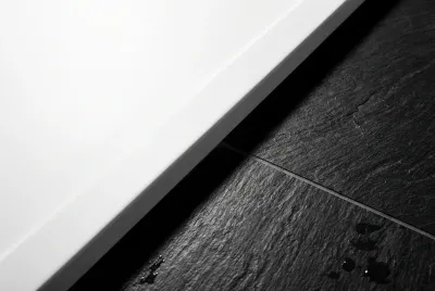 Gros plan de la jonction nette entre un receveur de douche blanc mat et un carrelage mural foncé, illustrant la précision de l'installation.