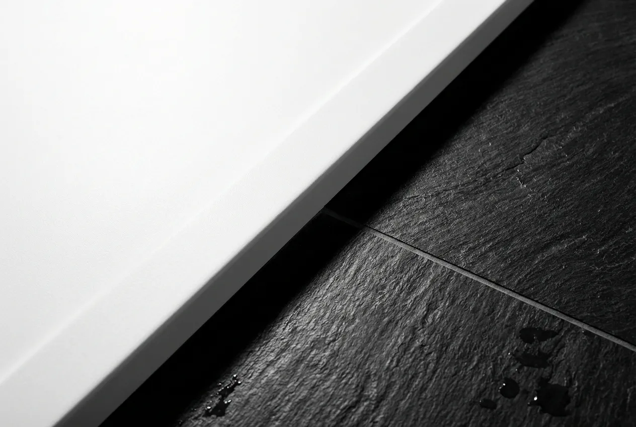 Gros plan de la jonction nette entre un receveur de douche blanc mat et un carrelage mural foncé, illustrant la précision de l'installation.
