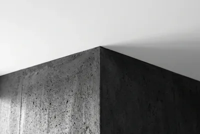 Gros plan géométrique et minimaliste de l'angle parfait entre un mur gris foncé et un plafond blanc.