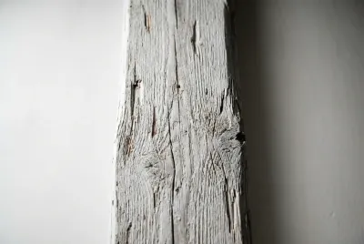 Gros plan texturé d'une poutre en bois blanchie, mettant en évidence le grain du bois sous la peinture blanche.